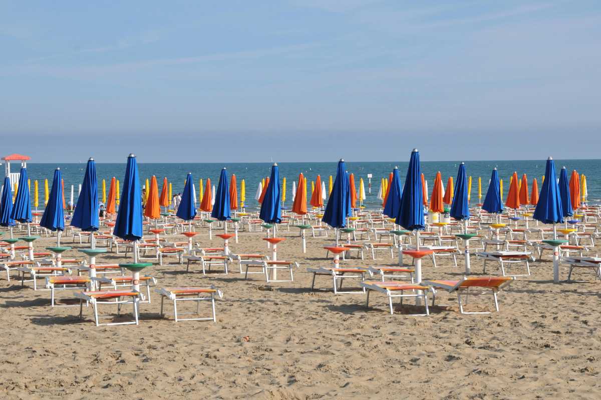 Tramonto sulla spiaggia di Lignano Sabbiadoro, con ombrelloni e persone che passeggiano